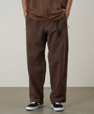 Model wearing walnut Gramicci Milton Pants and a brown shirt on a light-tone background.