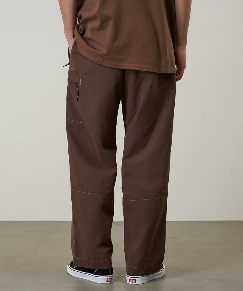 Model wearing walnut Gramicci Milton Pants and a brown shirt on a light-tone background.