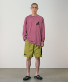 Model wearing field green Gramicci Guide Shorts and a red shirt on a light-tone background.