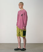 Model wearing field green Gramicci Guide Shorts and a red shirt on a light-tone background.