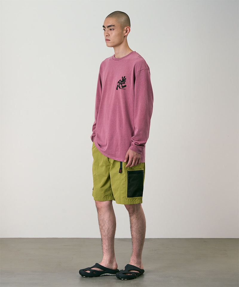 Model wearing field green Gramicci Guide Shorts and a red shirt on a light-tone background.