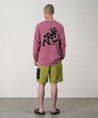 Back view of a model wearing field green Gramicci Guide Shorts and a red shirt on a light-tone background.