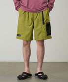 Model wearing field green Gramicci Guide Shorts and a red shirt on a light-tone background.