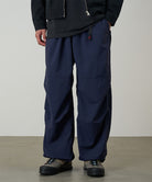 Model wearing british navy Gramicci Nylon Paneled Trek Pants and a black jacket on a light-tone background.