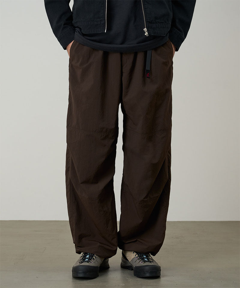 Model wearing chocolate colored Gramicci Nylon Paneled Trek Pants and a black jacket on a light-tone background.