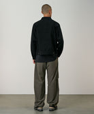 Back view of a model wearing granite colored Gramicci Nylon Paneled Trek Pants and a black jacket on a light-tone background.