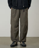 Model wearing granite colored Gramicci Nylon Paneled Trek Pants and a black jacket on a light-tone background.