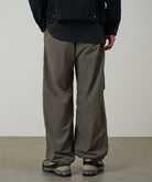 Back view of a model wearing granite colored Gramicci Nylon Paneled Trek Pants and a black jacket on a light-tone background.