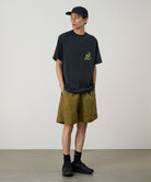 Model wearing artichoke colored Gramicci Nylon Reef Shorts and a black shirt on a light-tone background.