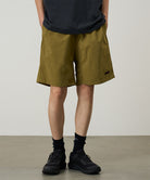 Model wearing artichoke colored Gramicci Nylon Reef Shorts and a black shirt on a light-tone background.