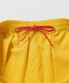 Close-up of banana colored Gramicci Nylon Reef Shorts with a red drawstring on a light-tone background.