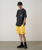 Model wearing a banana colored Gramicci Nylon Reef Short and a black shirt on a light-tone background.