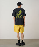 Back view of a model wearing a banana colored Gramicci Nylon Reef Short and a black shirt on a light-tone background.