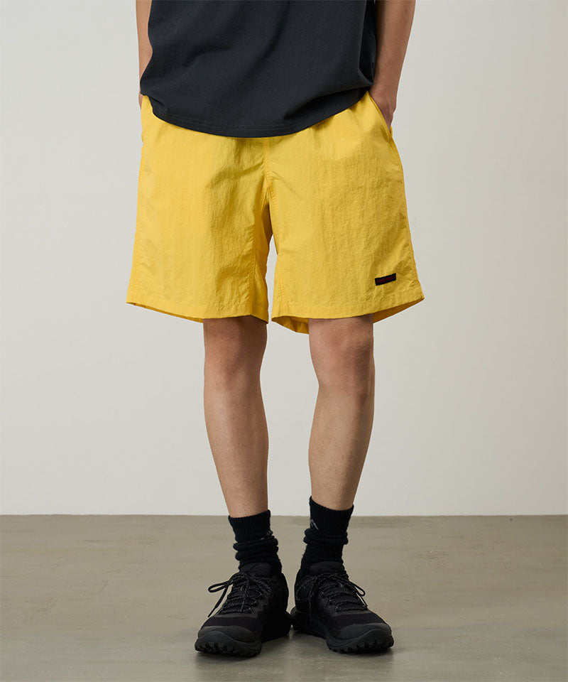 Model wearing banana colored Gramicci Nylon Reef Shorts and a black shirt on a light-tone background.
