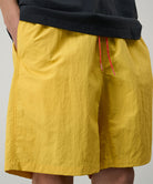 Model wearing banana colored Gramicci Nylon Reef Shorts and a black shirt on a light-tone background.