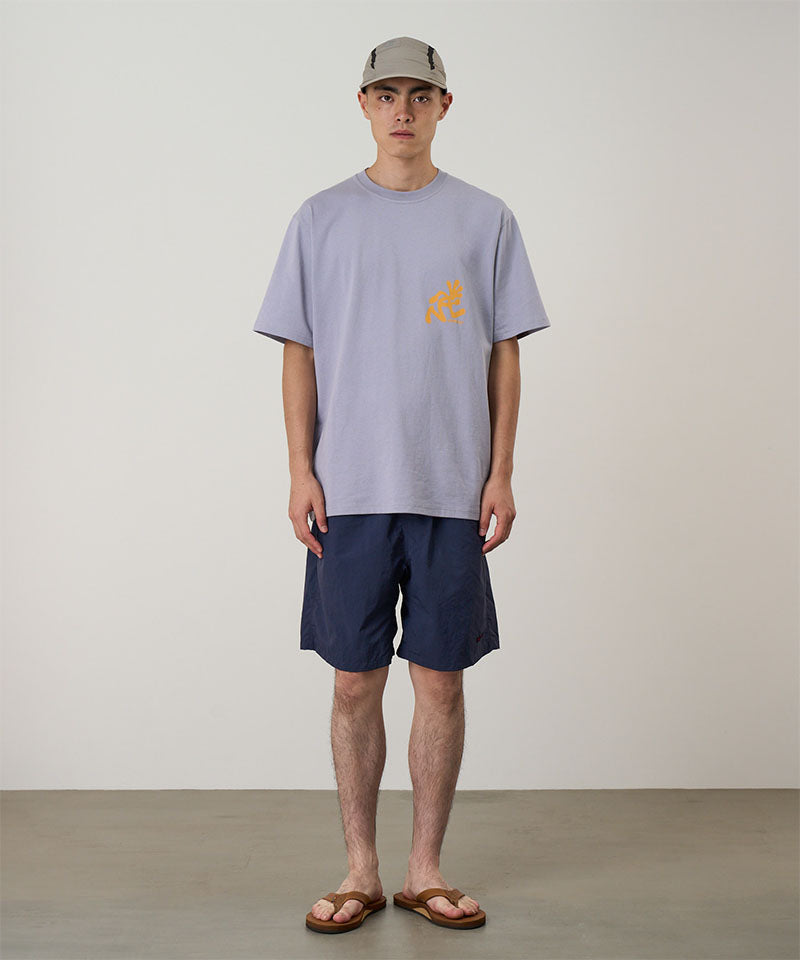 Model wearing british navy Gramicci Nylon Reef Shorts and a lavender shirt on a light-tone background.