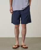 Model wearing british navy Gramicci Nylon Reef Shorts and a lavender shirt on a light-tone background.