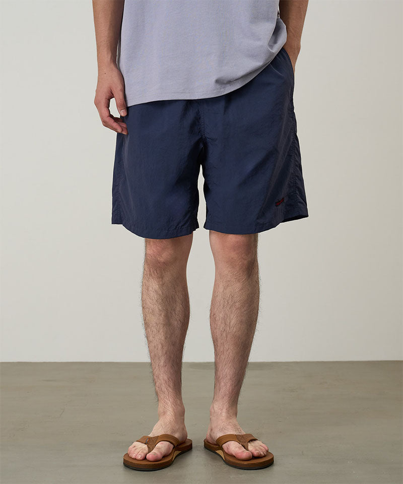 Model wearing british navy Gramicci Nylon Reef Shorts and a lavender shirt on a light-tone background.
