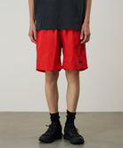 Model wearing burnt orange Gramicci Nylon Reef Shorts and a black shirt on a light-tone background.