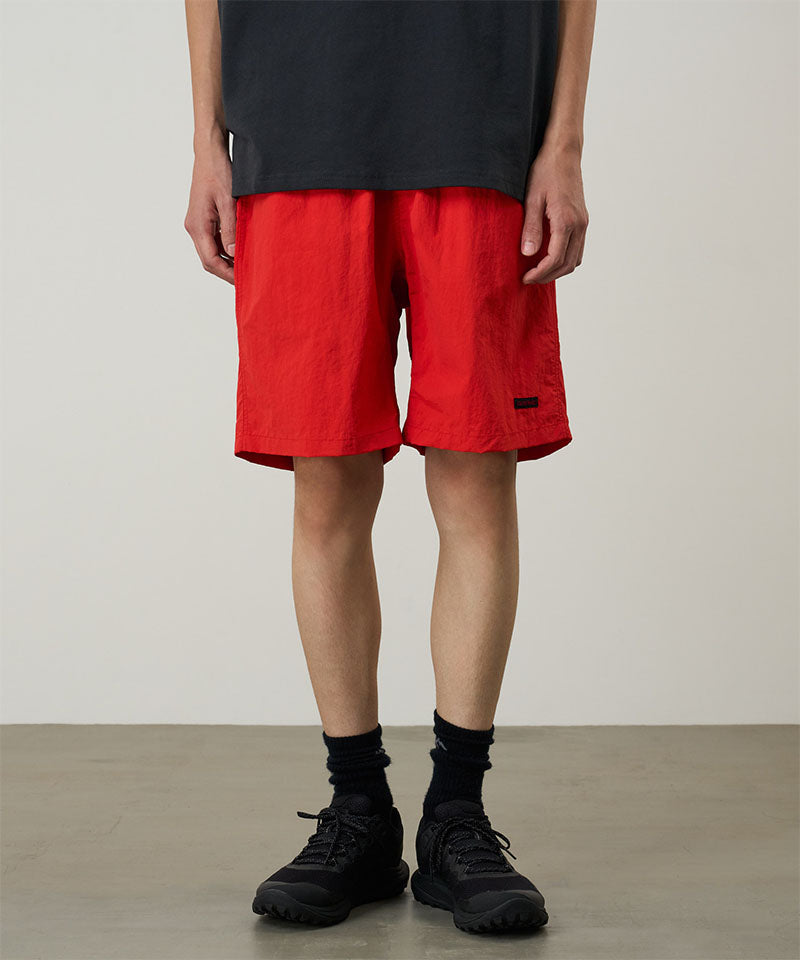 Model wearing burnt orange Gramicci Nylon Reef Shorts and a black shirt on a light-tone background.