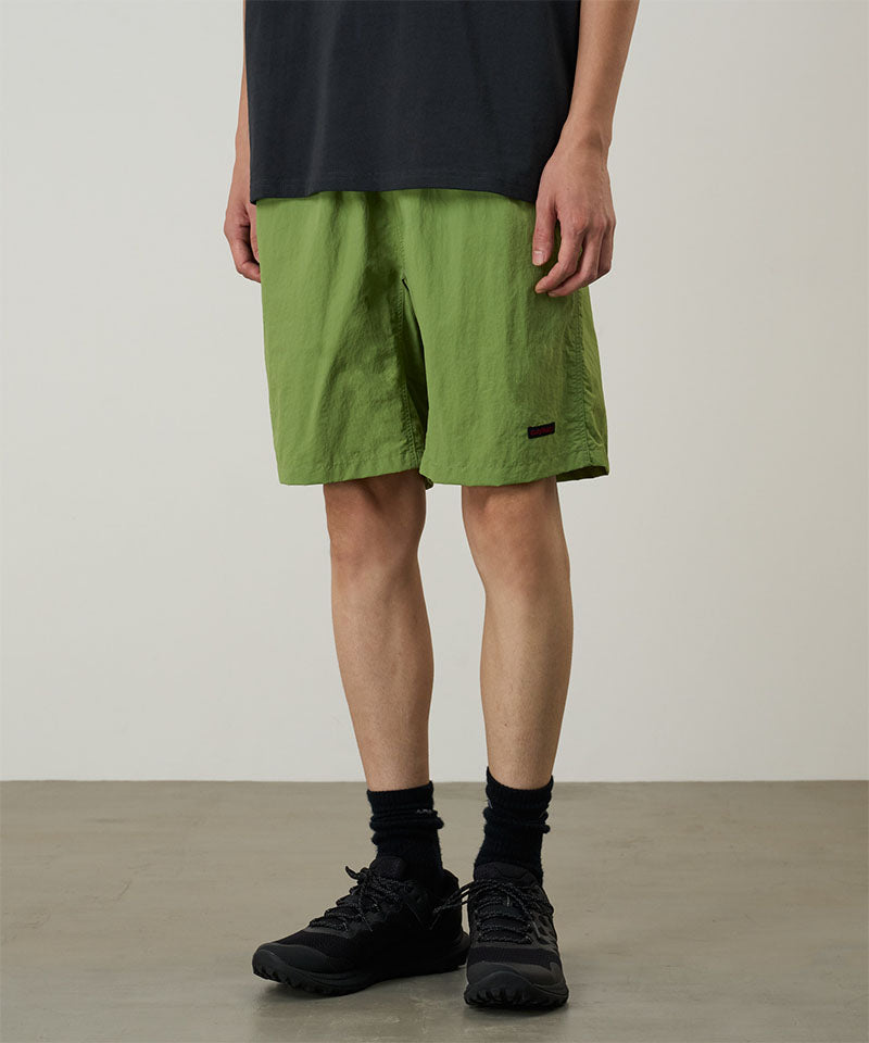 Model wearing jade green Gramicci Nylon Reef Shorts and a black shirt on a light-tone background.