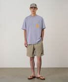 Model wearing milk tea colored Gramicci Nylon Reef Shorts and a lavender shirt on a light-tone background.