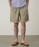 Model wearing milk tea colored Gramicci Nylon Reef Shorts and a lavender shirt on a light-tone background.