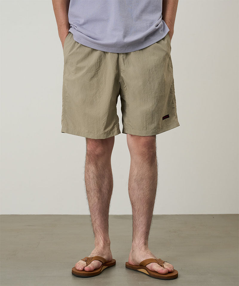 Model wearing milk tea colored Gramicci Nylon Reef Shorts and a lavender shirt on a light-tone background.
