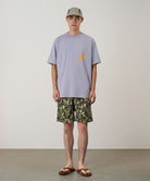 Model wearing olive camo Gramicci Nylon Reef Shorts and a lavender shirt on a light-tone background.
