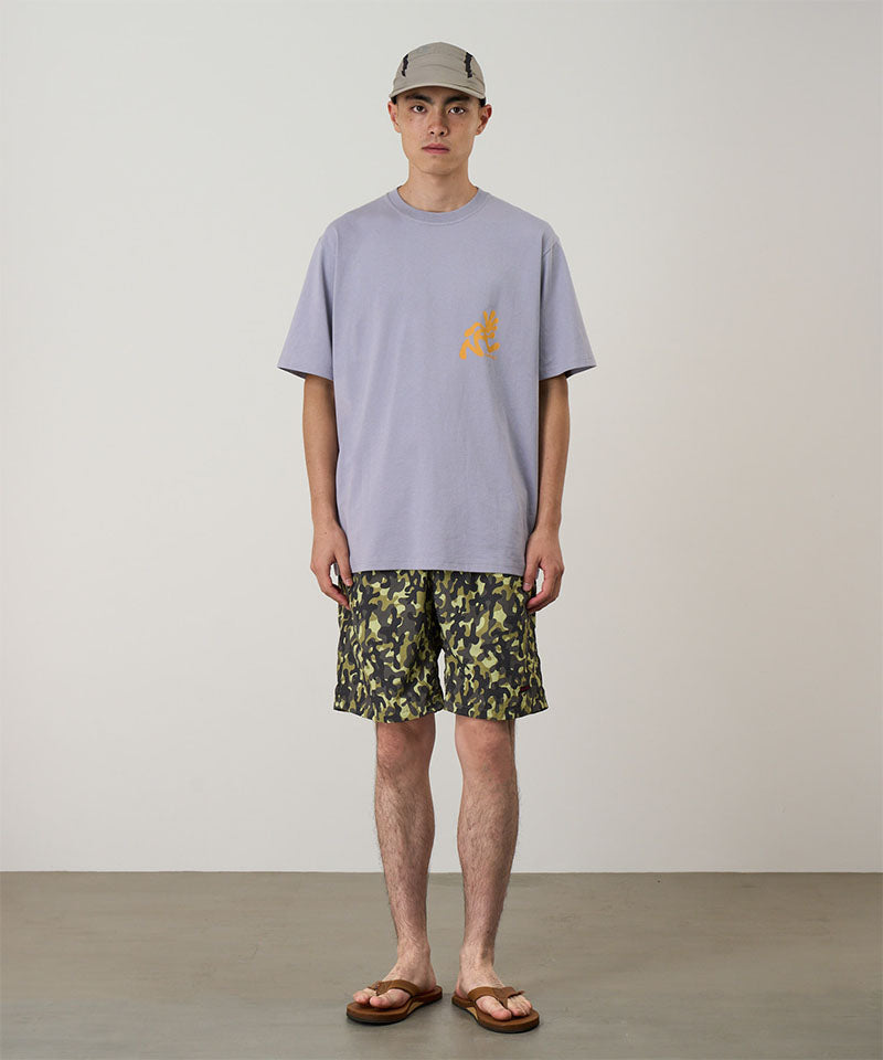Model wearing olive camo Gramicci Nylon Reef Shorts and a lavender shirt on a light-tone background.