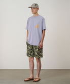 Model wearing olive camo Gramicci Nylon Reef Shorts and a lavender shirt on a light-tone background.