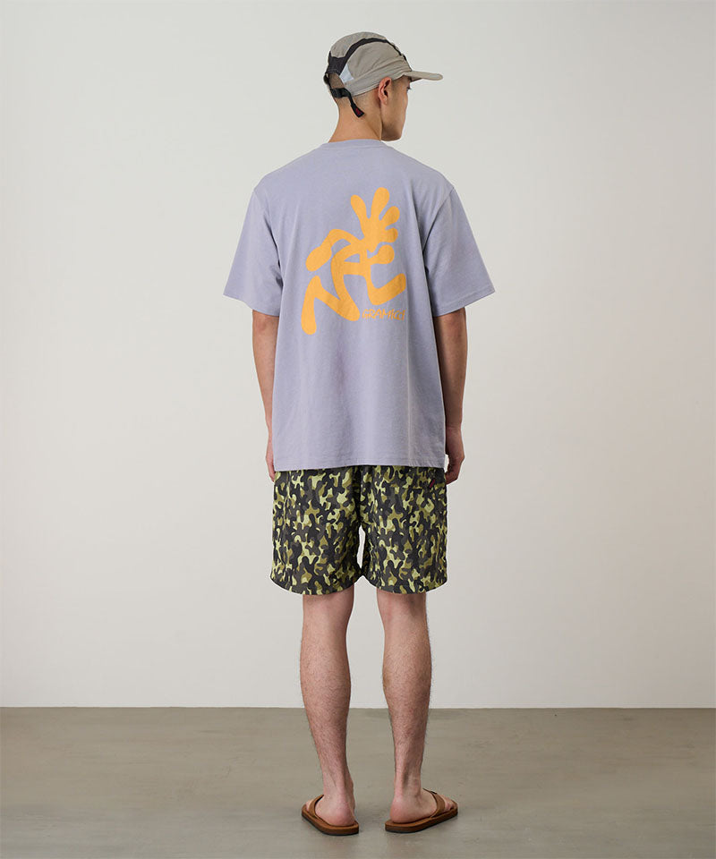 Back view of a model wearing olive camo Gramicci Nylon Reef Shorts and a lavender shirt on a light-tone background.