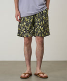Model wearing olive camo Gramicci Nylon Reef Shorts and a lavender shirt on a light-tone background.