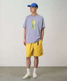 Model wearing banana colored Gramicci Nylon Packable G-Shorts and a lavender shirt on a light-tone background.
