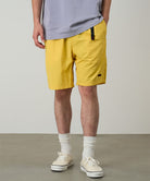 Model wearing banana colored Gramicci Nylon Packable G-Shorts and a lavender shirt on a light-tone background.