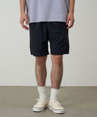 Model wearing black Gramicci Nylon Packable G-Shorts and a lavender shirt on a light-tone background.