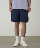 Model wearing british navy Gramicci Nylon Packable G-Shorts and a lavender shirt on a light-tone background.