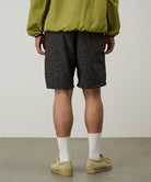 Back view of a model wearing brown leaf colored Gramicci Nylon Packable G-Short and a olive jacket on a light-tone background.