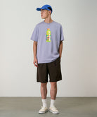 Model wearing chocolate colored Gramicci Nylon Packable G-Shorts and a lavender shirt on a light-tone background.