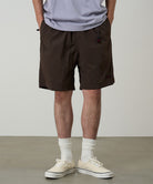 Model wearing chocolate colored Gramicci Nylon Packable G-Shorts and a lavender shirt on a light-tone background.