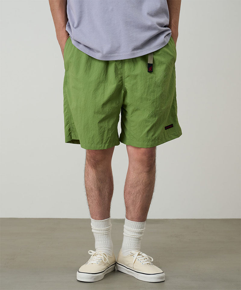 Model wearing jade green Gramicci Nylon Packable G-Shorts and a lavender shirt on a light-tone background.