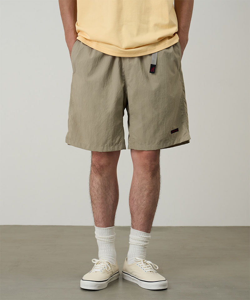 Model wearing milk tea colored Gramicci Nylon Packable G-Shorts and a mango colored shirt on a light-tone background.