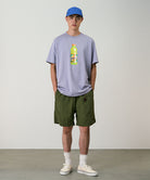 Model wearing olive Gramicci Nylon Packable G-Shorts and a lavender shirt on a light-tone background.