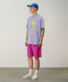 Model wearing bright plum colored Gramicci Nylon Packable G-Short and a lavender shirt on a light-tone background.