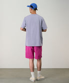 Back view of a model wearing bright plum colored Gramicci Nylon Packable G-Short and a lavender shirt on a light-tone background.