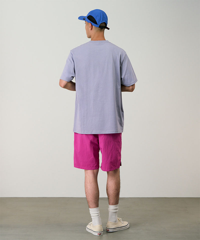 Back view of a model wearing bright plum colored Gramicci Nylon Packable G-Short and a lavender shirt on a light-tone background.
