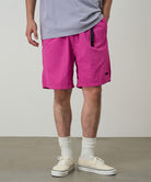 Model wearing bright plum colored Gramicci Nylon Packable G-Short and a lavender shirt on a light-tone background.