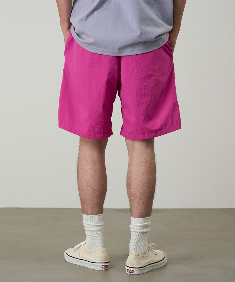 Back view of a model wearing bright plum colored Gramicci Nylon Packable G-Short and a lavender shirt on a light-tone background.