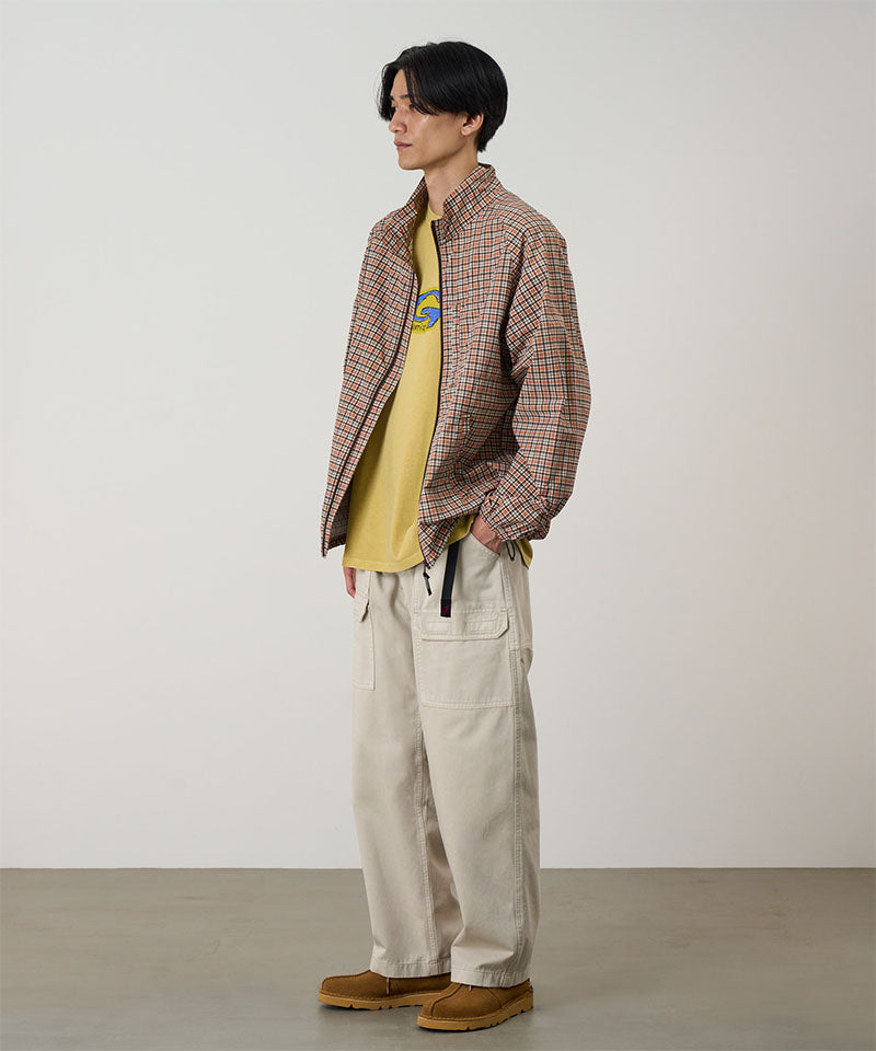 Model wearing sand pigment Gramicci EQT Pant and a plaid jacket on a light-tone background.