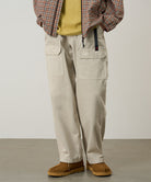 Model wearing sand pigment Gramicci EQT Pant and a plaid jacket on a light-tone background.